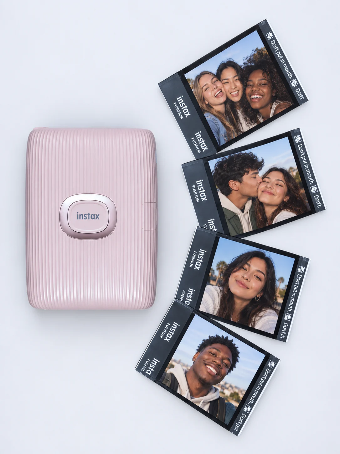 Pink Instax printer beside mini photo prints of friends and a couple.