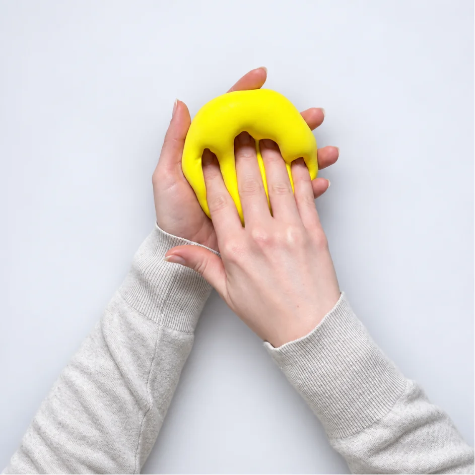 Hands stretching and shaping bright yellow foam clay.